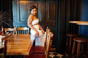 African american woman, retro hairstyle in white dress at restaurant. photo