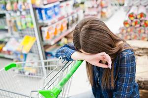 Shopping woman looking at the shelves in the supermarket.  Portrait of a young girl in a market store with shopping cart. photo