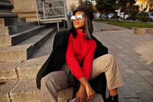 African american fashion girl in coat and newsboy cap, sunglasses posed at street. photo