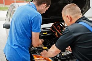 Car repair and maintenance theme. Two mechanics in uniform working in auto service, checking engine. photo