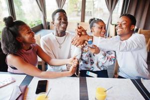 Happy african friends sitting and chatting in cafe. Group of black peoples meeting and play games by hands in restaurant. photo