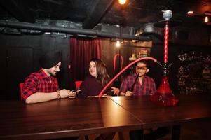 Group of indian friends sitting at lounge bar, smoke hookah and having rest. photo