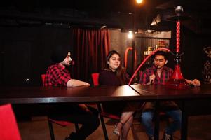 Group of indian friends sitting at lounge bar, smoke hookah and having rest. photo