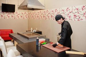 chef profesional vestido de negro haciendo sushi y rollos en la cocina de un restaurante de comida tradicional japonesa. foto