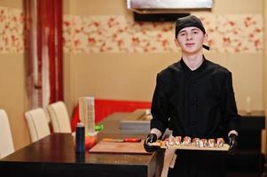 Professional chef wear in black with sushi and rolls in a restaurant of japanese traditional food. photo