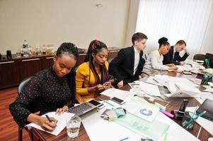 Multiracial business team addressing meeting around boardroom table, working together and write something on papers. photo