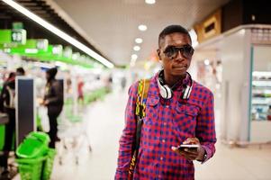 African american man in checkered shirt with suitcase and backpack. Black man against cashier supermarket. photo