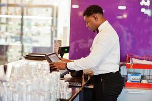 African american bartender wear on bow tie using cash terminal screen at bar. photo