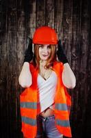 Engineer woman in orange protect helmet and building jacket against wooden background. photo