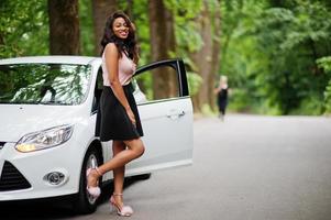 mujer afroamericana posó contra un auto blanco en un camino forestal. foto