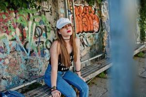 Stylish casual hipster girl in cap  and jeans wear against large graffiti wall. photo