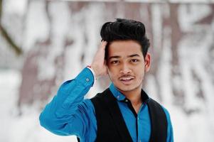 un joven indio casual con camisa azul y chaleco negro posó en el día de invierno. foto