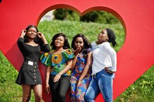 Group of four african american girls against big red heart outdoor sending air kisses. photo