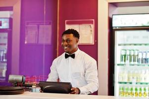 African american bartender wear on bow tie using cash terminal screen at bar. photo