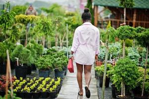 African woman in pink large shirt posed at garden with seedlings. photo