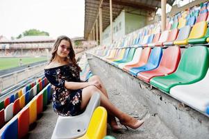 Portrait of a young beutiful girl in dress and sunglasses sitting on the tribunes in stadium. photo