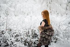 chica pelirroja con abrigo de piel caminando en el parque nevado de invierno. foto