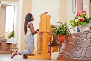 African american woman praying in the church. Believers meditates in the cathedral and spiritual time of prayer. Afro girl kneeling and confession. photo