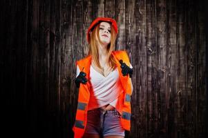 Engineer woman in orange protect helmet and building jacket against wooden background. photo