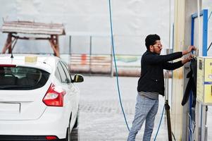 South asian man or indian male washing his white transportation on car wash. photo