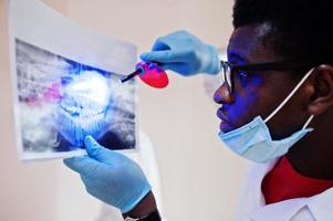 Dentist office and doctor practice concept. Close uo of hands professional african american doctor at dentistry medical pointing on teeth X-ray. photo