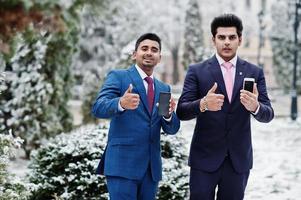Two elegant indian fashionable mans model on suit posed at winter day and show thumbs up and mobile phone. photo