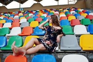 retrato de una joven hermosa vestida y gafas de sol sentada en las tribunas del estadio. foto