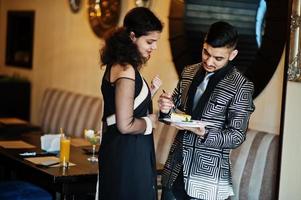 Lovely indian couple in love, wear at saree and elegant suit, posed on restaurant, hold plate with cake. photo