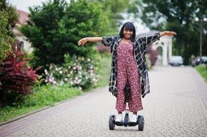 hermosa mujer afroamericana usando segway o hoverboard. chica negra en scooter eléctrico autoequilibrado de doble rueda. foto