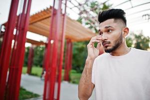 Stylish indian beard man at pink t-shirt. India model posed under red arch at park of city. photo