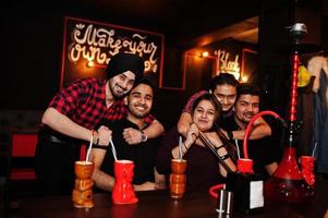 Group of indian friends having fun and rest at night club, drinking cocktails and smoke hookah. photo