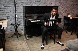 Strong powerful african american man in black suit sitting against piano. photo