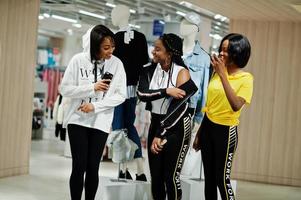 Three afican american women in tracksuits shopping at sportswear mall against mannequin. Sport store theme. photo