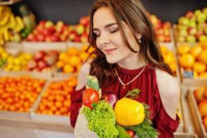 Girl in red holding different vegetables on fruits store. photo