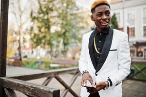 elegante hombre afroamericano guapo en traje blanco con teléfono móvil a mano. foto