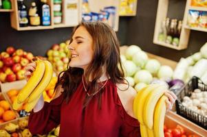 Girl in red holding bananas on fruits store. photo
