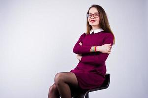 Portrait of a young woman in purple dress and glasses sitting on the chair in the studio. photo