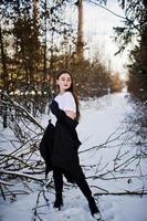 modelo morena de piernas largas de moda en un largo manto negro posado al aire libre en el día de invierno. foto