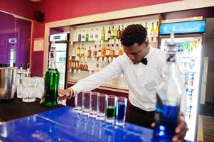 African american bartender at bar making coctails on shots. Alcoholic beverage preparation. photo