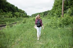 retrato de una hermosa chica rubia con camisa de tartán caminando con un mapa en el campo. foto