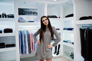 hermosa chica morena en la boutique de la tienda de ropa en vestido gris. foto