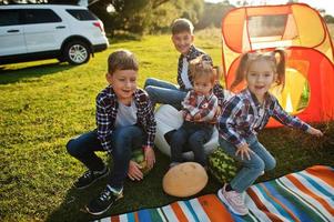 Four kids spending time together. Outdoor picnic blanket, sitting with watermelons. photo