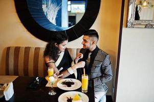 Lovely indian couple in love, wear at saree and elegant suit, posed on restaurant. Woman tied tie on her man. photo