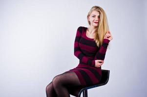 Portrait of a young woman in striped purple dress sitting on the chair in the studio. photo