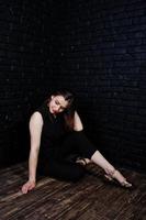 Portrait of a beautiful brunette girl in black jumpsuit sitting and posing in the studio. photo