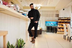 Arab man wear on black jeans jacket and eyeglasses in cafe drink coffee at bar. Stylish and fashionable arabian model guy. photo