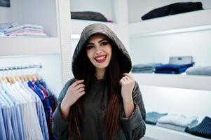 hermosa chica morena en la boutique de la tienda de ropa en chaqueta de invierno con capucha. foto