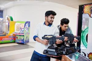 Two asian guys compete on shooter simulator game arcade machine. photo