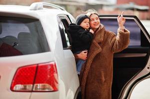 la joven madre y el niño se paran cerca de su auto todoterreno. concepto de conducción segura. foto