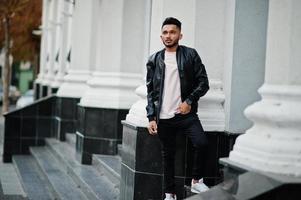 Stylish indian beard man at black leather jacket. India model posed outdoor at streets of city. photo